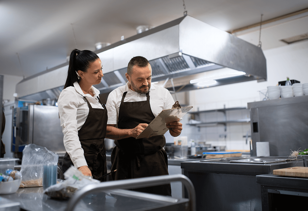 Two kitchen staff do a temperature log using a clipboard