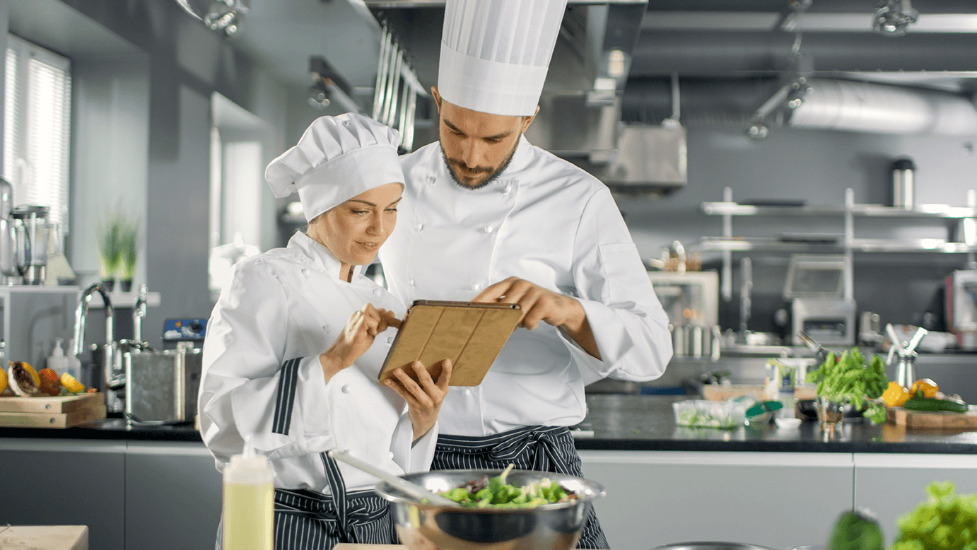a chef shows a colleague how to complete an audit using his tablet