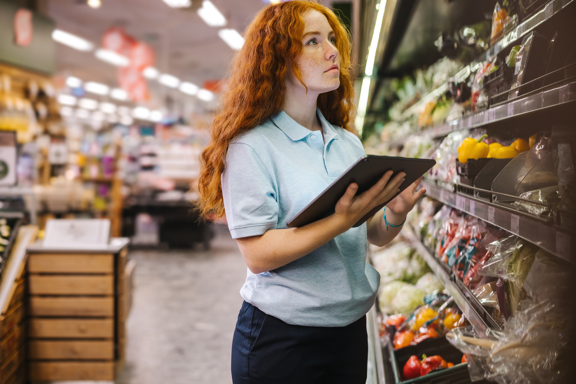 supermarket employee looks at shelves while holding tablet supermarket employee looks at shelves while holding tablet